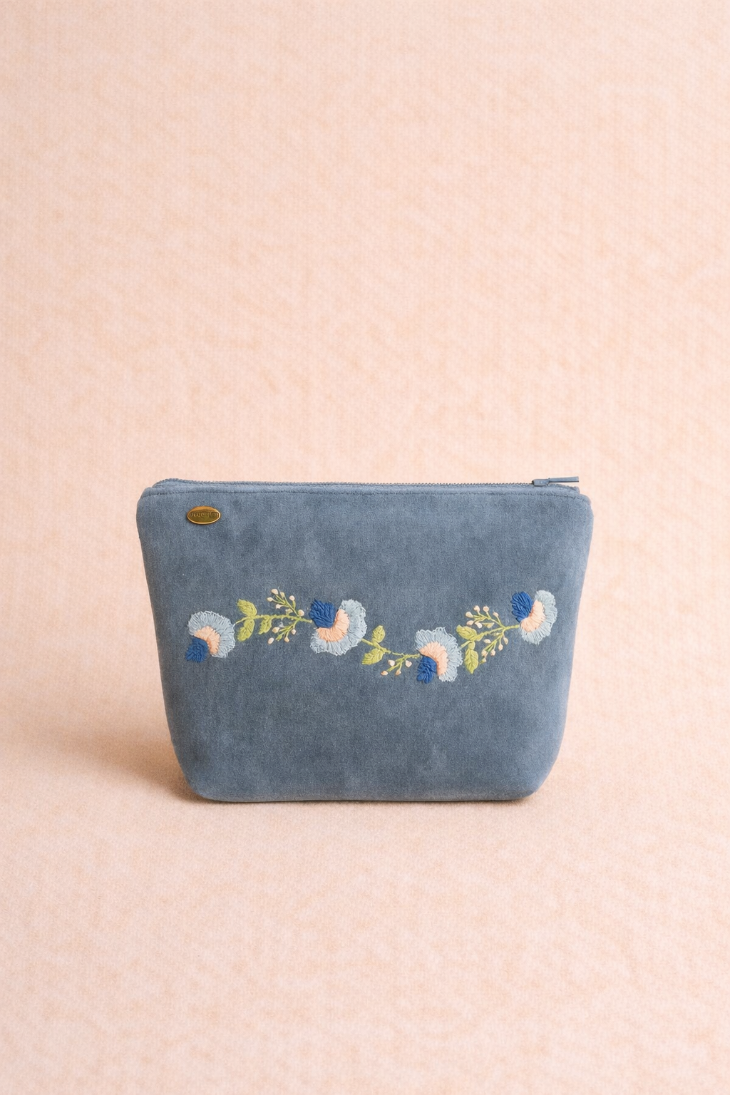 Blue fabric zip pouch with hand-embroidered floral vine motif in peach, ivory, green, and navy