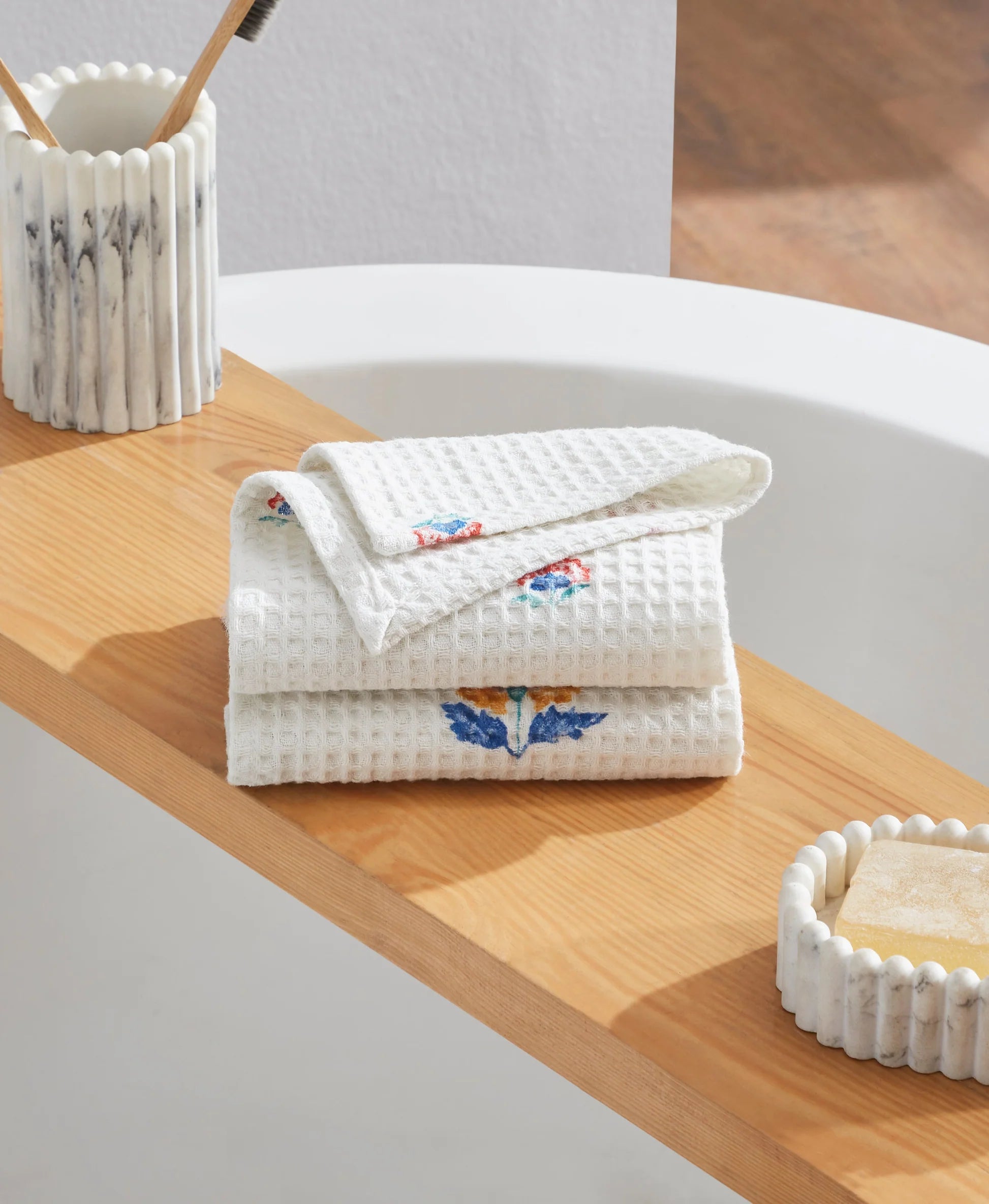 Stack of white towels with floral patterns on a wooden surface next to a bathtub.