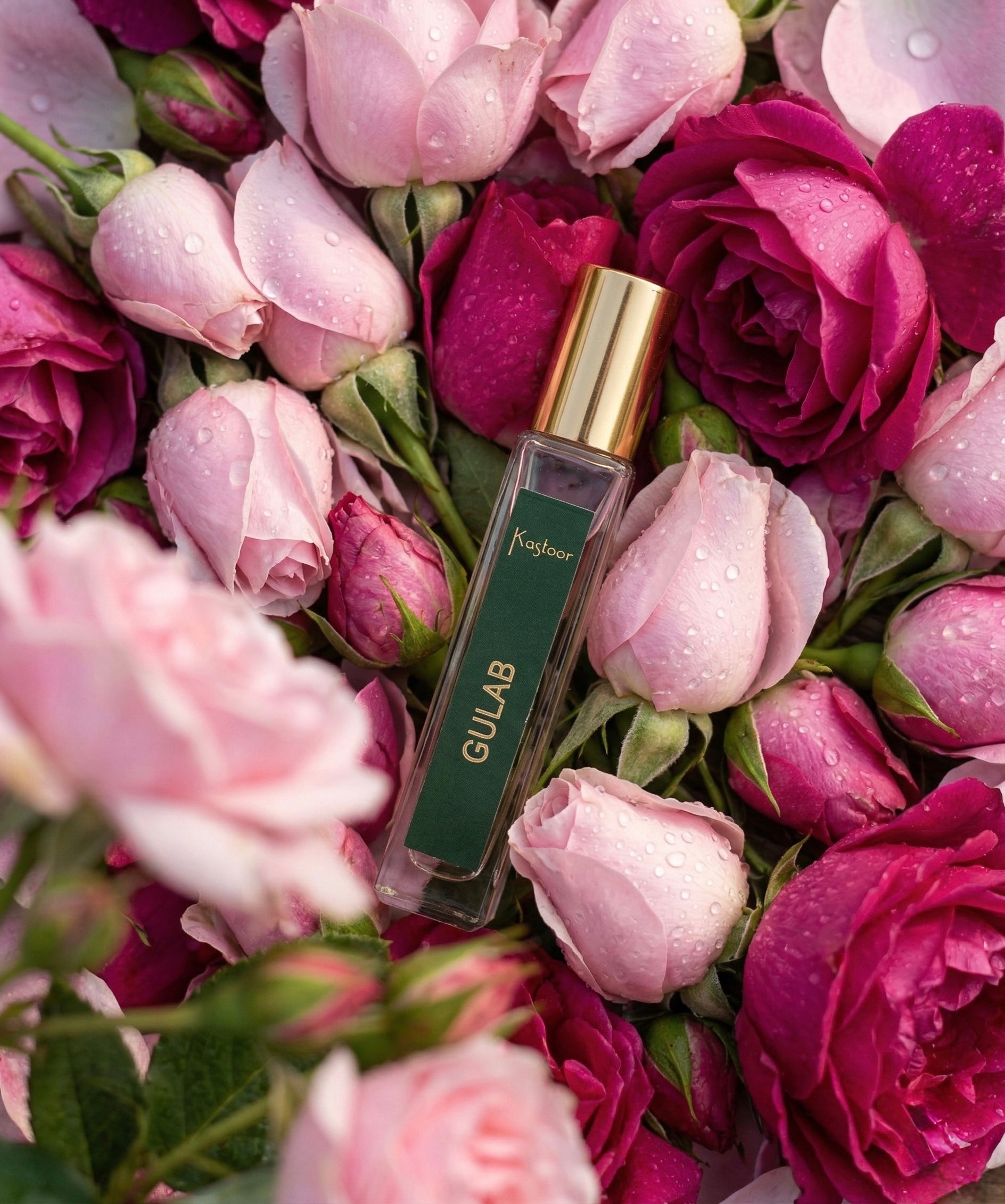 Perfume bottle labeled 'Gulab' surrounded by pink and purple roses with water droplets.