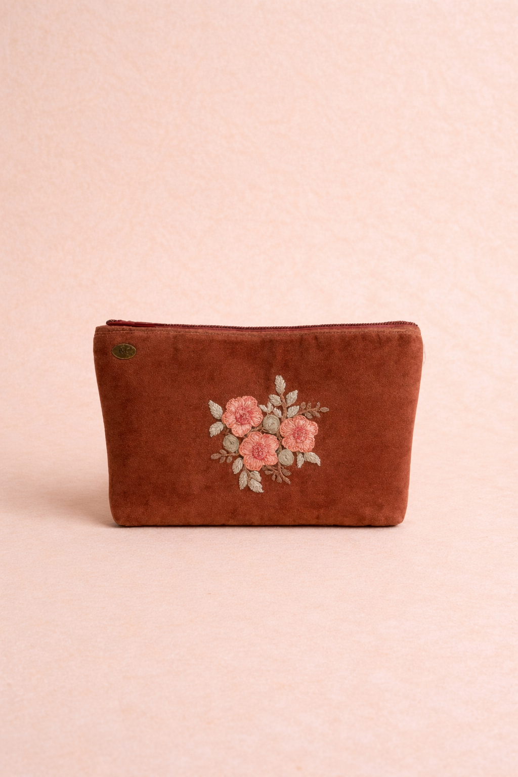 Brown pouch with floral embroidery on a beige background