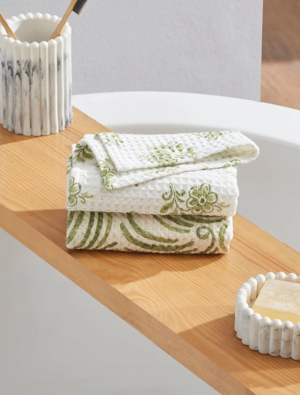 Folded green and white patterned towel on a wooden surface with a marble-patterned candle and soap dish.