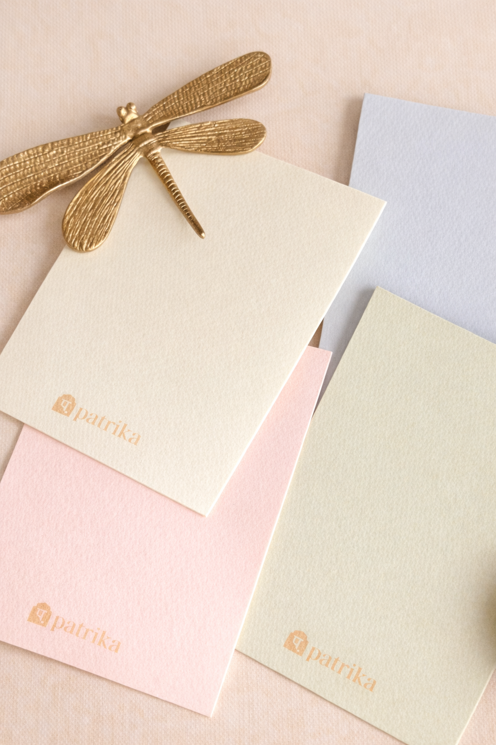 Pastel-colored envelopes with a gold dragonfly accessory on a matching pink background