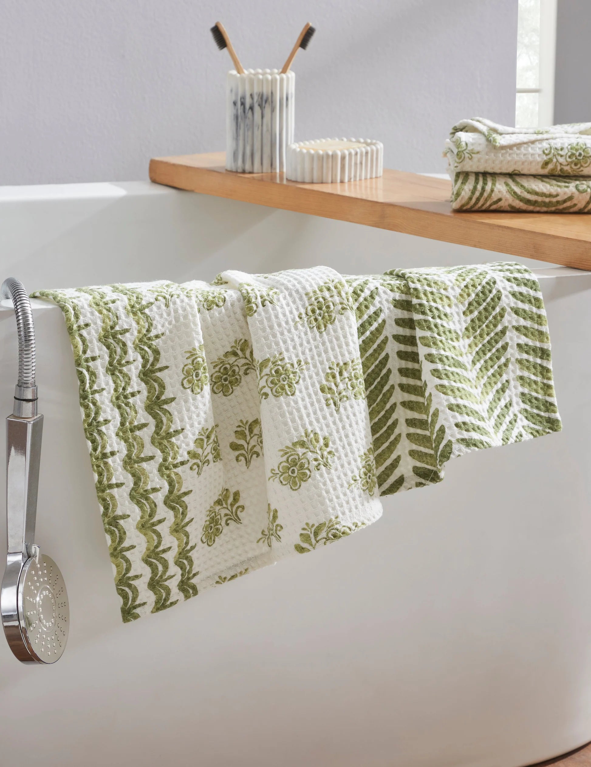 Green and white patterned towel hanging over a bathtub with a shelf in the background.