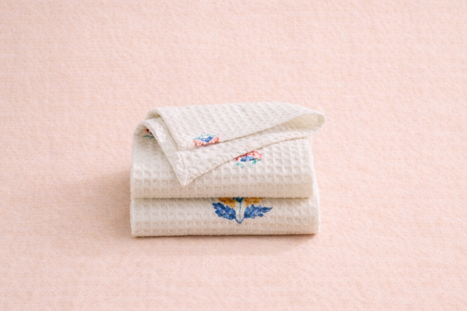 Folded ivory cotton waffle face towels with hand block-printed floral motifs in blue, mustard, and coral