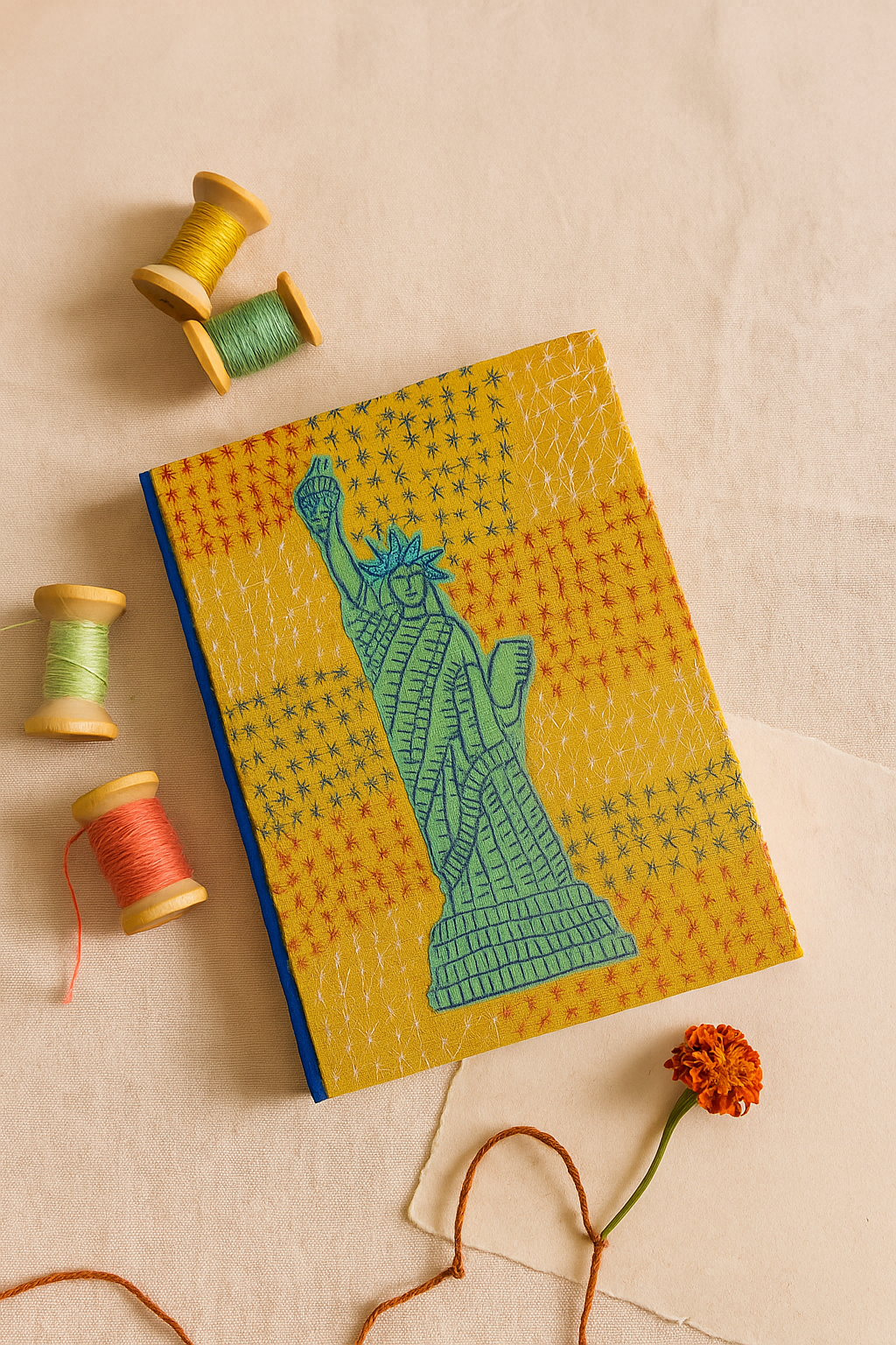 Notebook with Statue of Liberty design on a beige background with spools of thread and a flower.