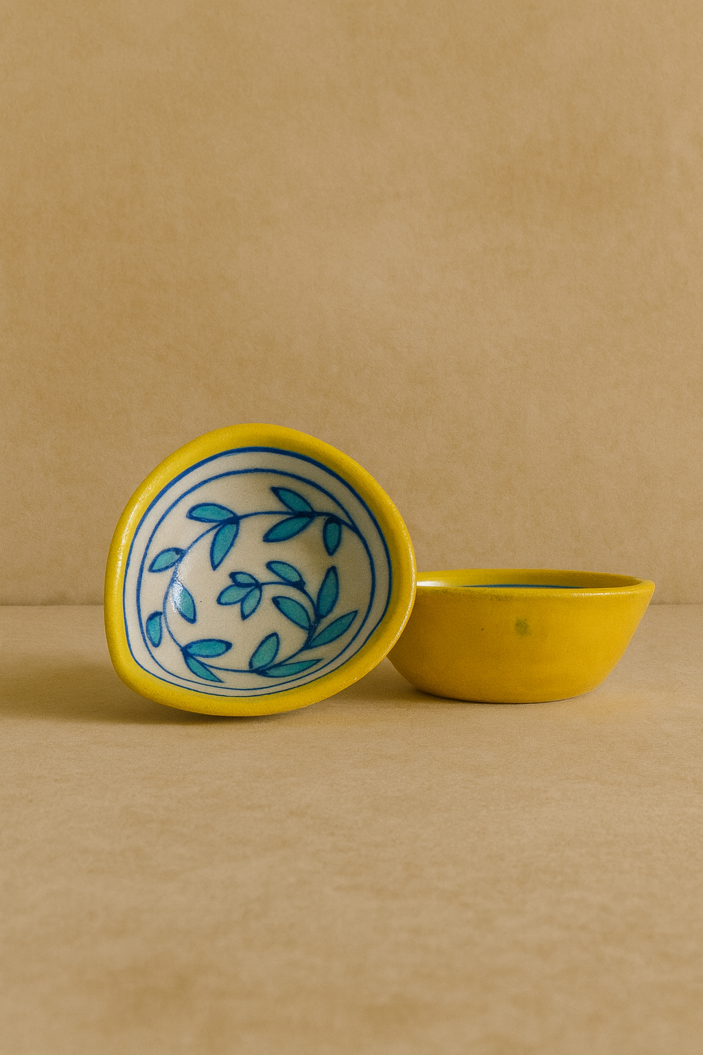 Yellow ceramic diya with blue leaf pattern on a beige background